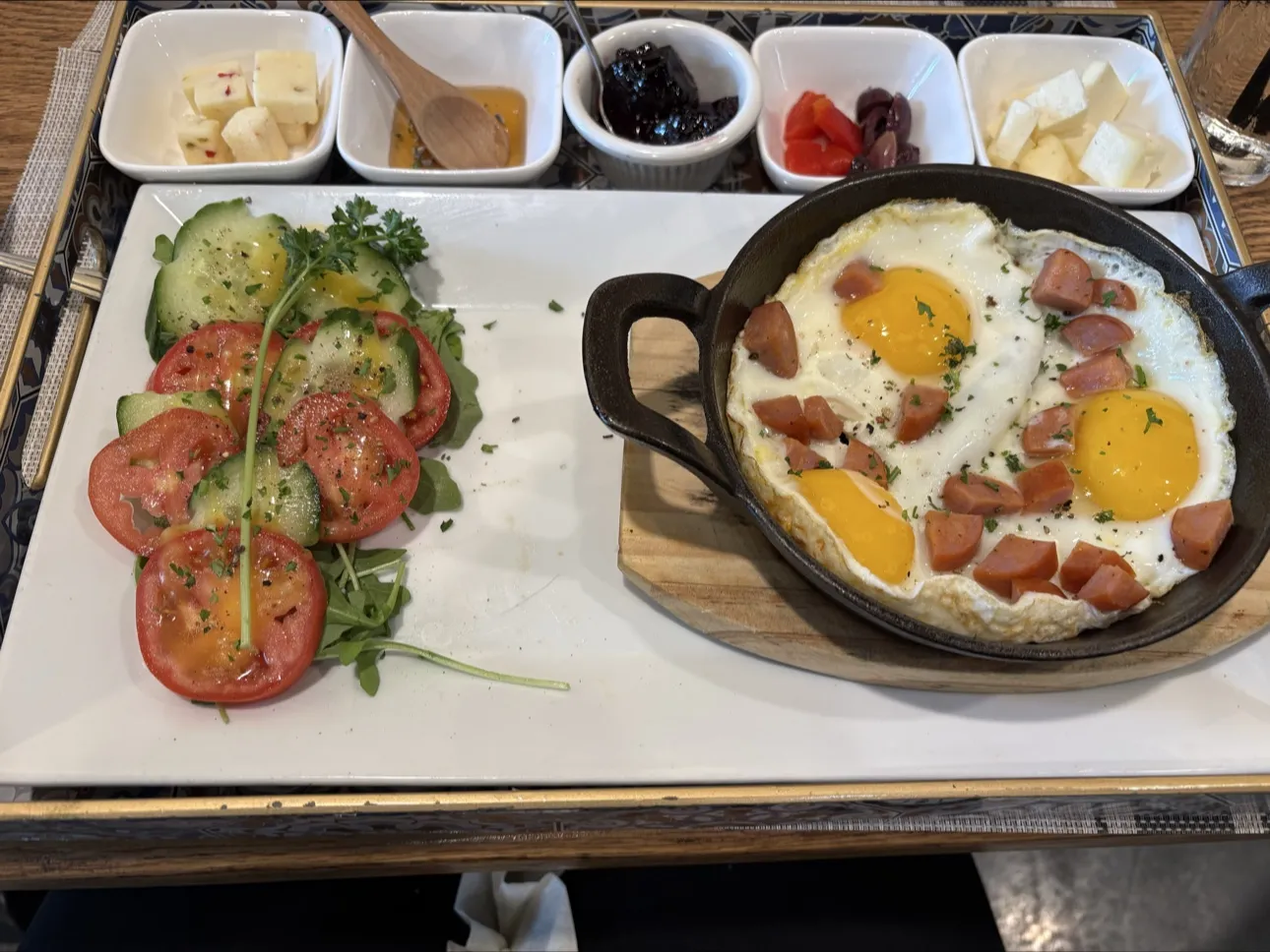 Ottoman breakfast: eggs and sausage in a skillet with tomato and cucumber salad, olives, cheese and honey